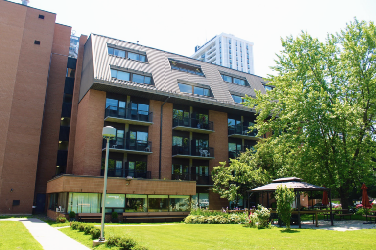 Exterior view of the Meighen Retirement Residence building with landscaped grounds, trees, and a gazebo in the courtyard.
