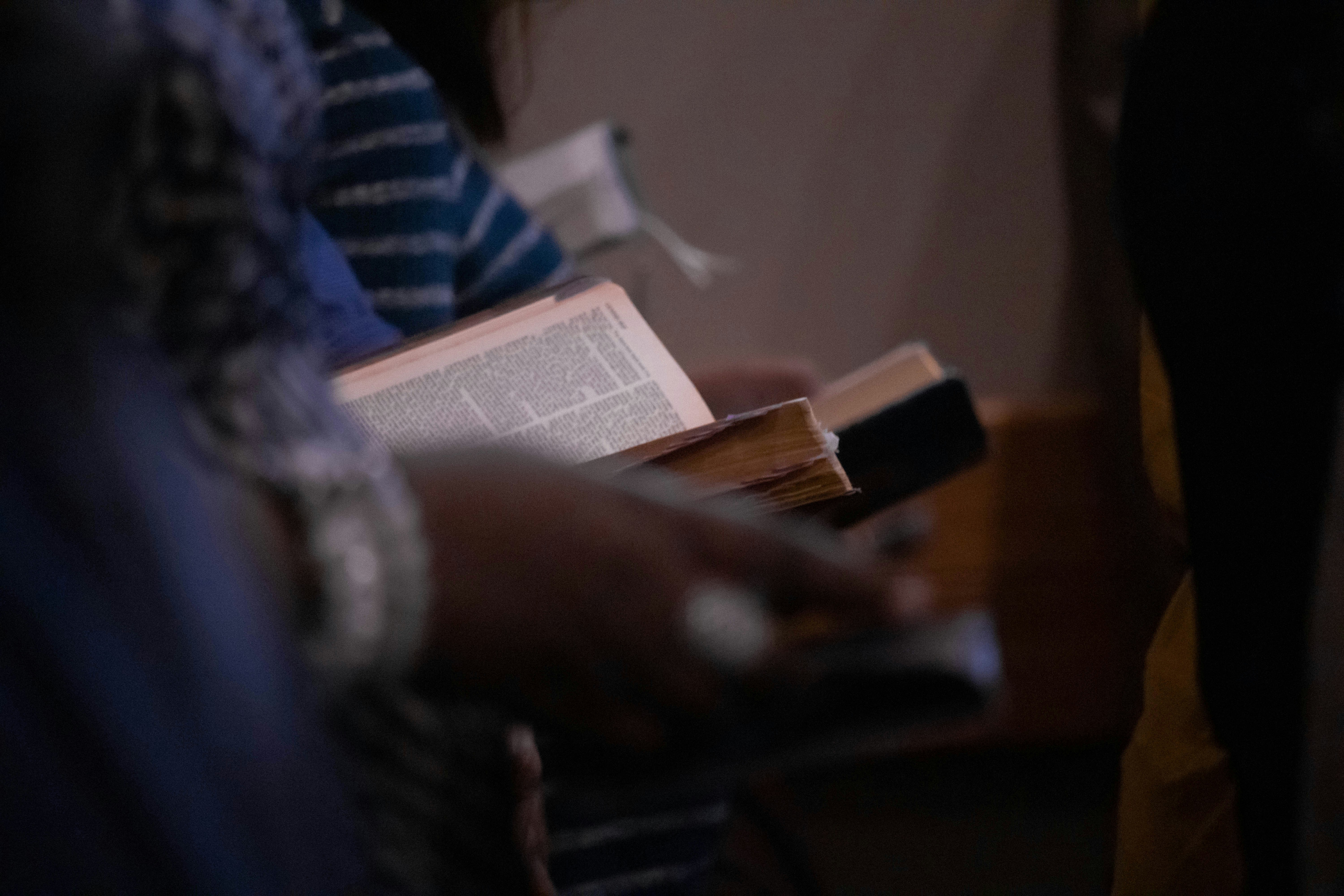 Close-up of a person holding and reading a Bible during a worship service in a softly lit setting.